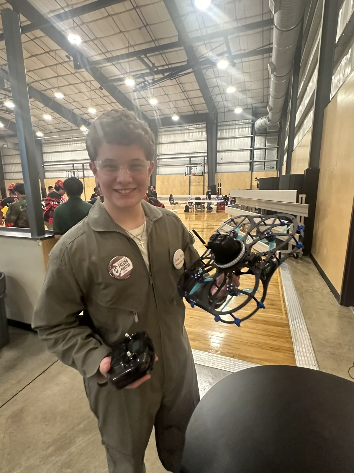 Henry in a flight suit holding a caged competition drone at a robotics event