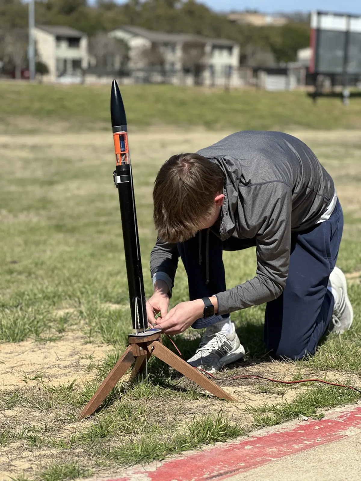 Charlie kneeling to set up a custom-built model rocket on its launch pad in a field